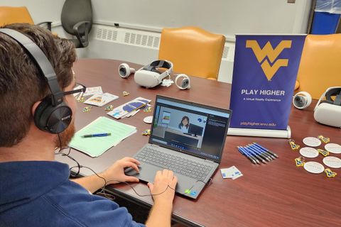 Photo of student playing laptop alternative elearning game with Play Higher popup banner on table.
