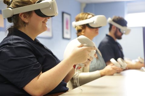 Photograph of people using virtual reality with Play Higher popup banner in front and Flying WV logo on the wall