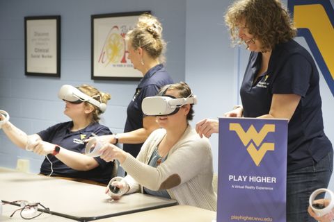 Photograph of people using virtual reality and staff helping users with Play Higher popup banner in front and Flying WV logo on the wall